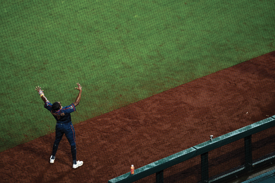 photo from above of man in uniform on side of baseball field raising both arms to the sky