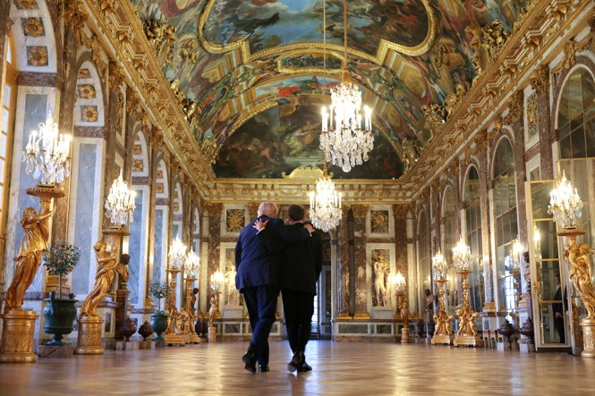 President Trump stands beside French President Emmanuel Macron as he receives a tour of a very ornate room in the Chateau de Versailles.