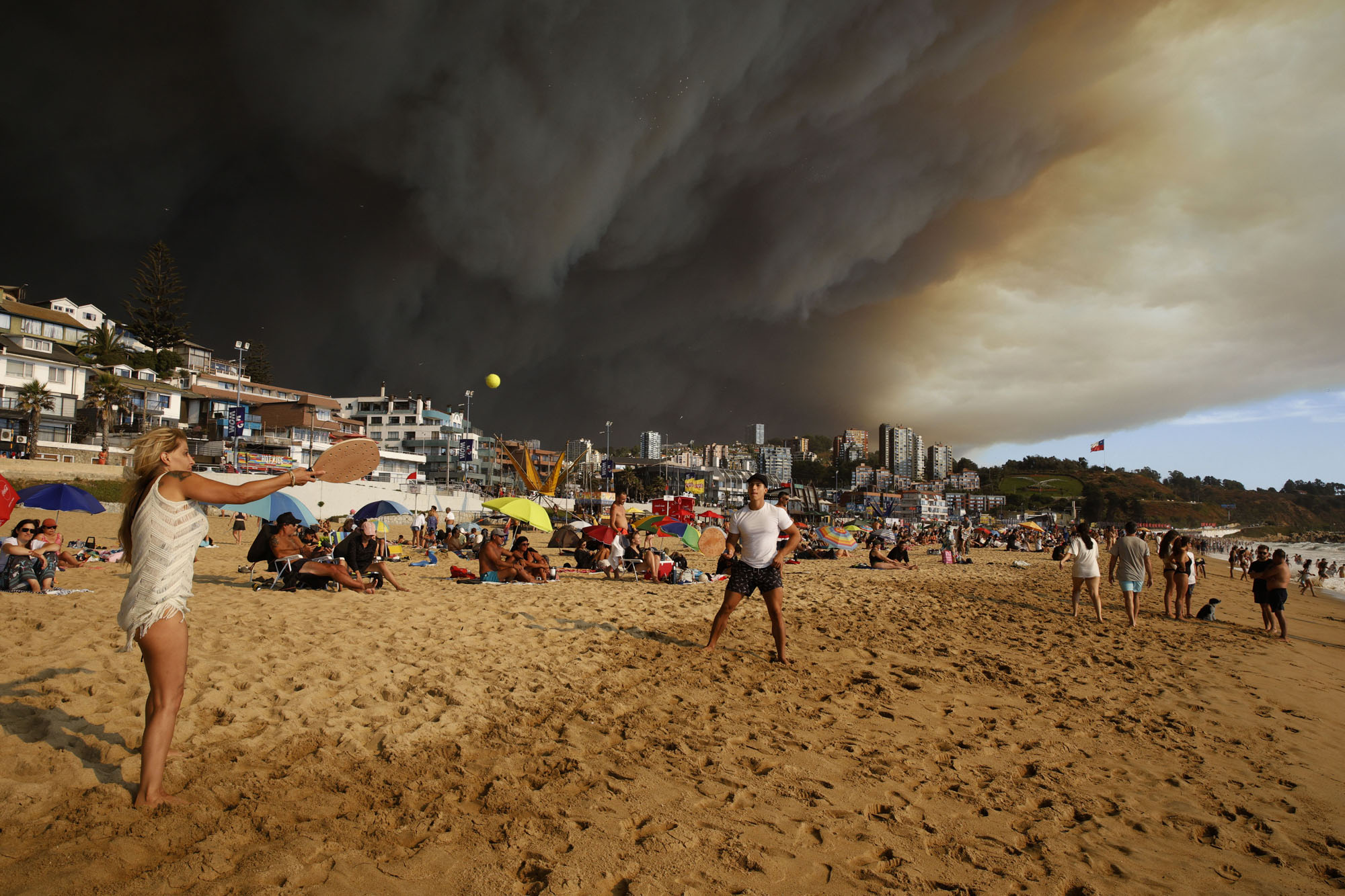 Vacationers play paddleball on a beach backdropped by a darkening sky caused by smoke from nearby forest fires, in Viña del Mar, Chile, on February 2, 2024.