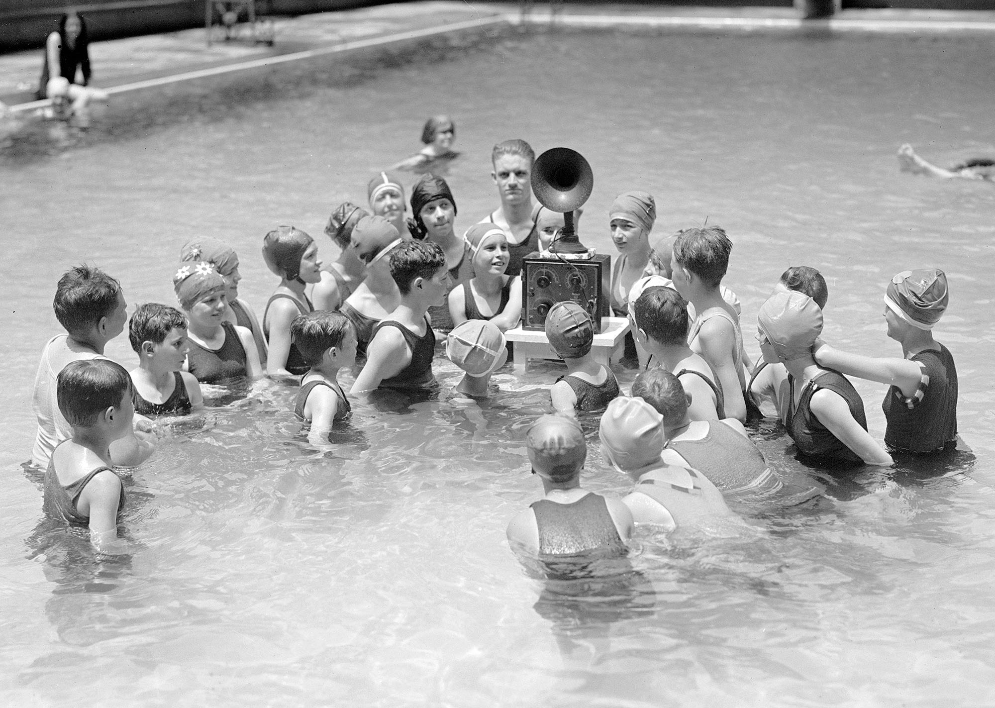 Children listen to a battery-powered radio receiver that is set on a table in a swimming pool in Washington, D.C., in July 1924.
