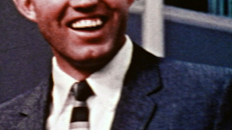 A man wearing a suit laughs, and only the bottom half of his face is visible