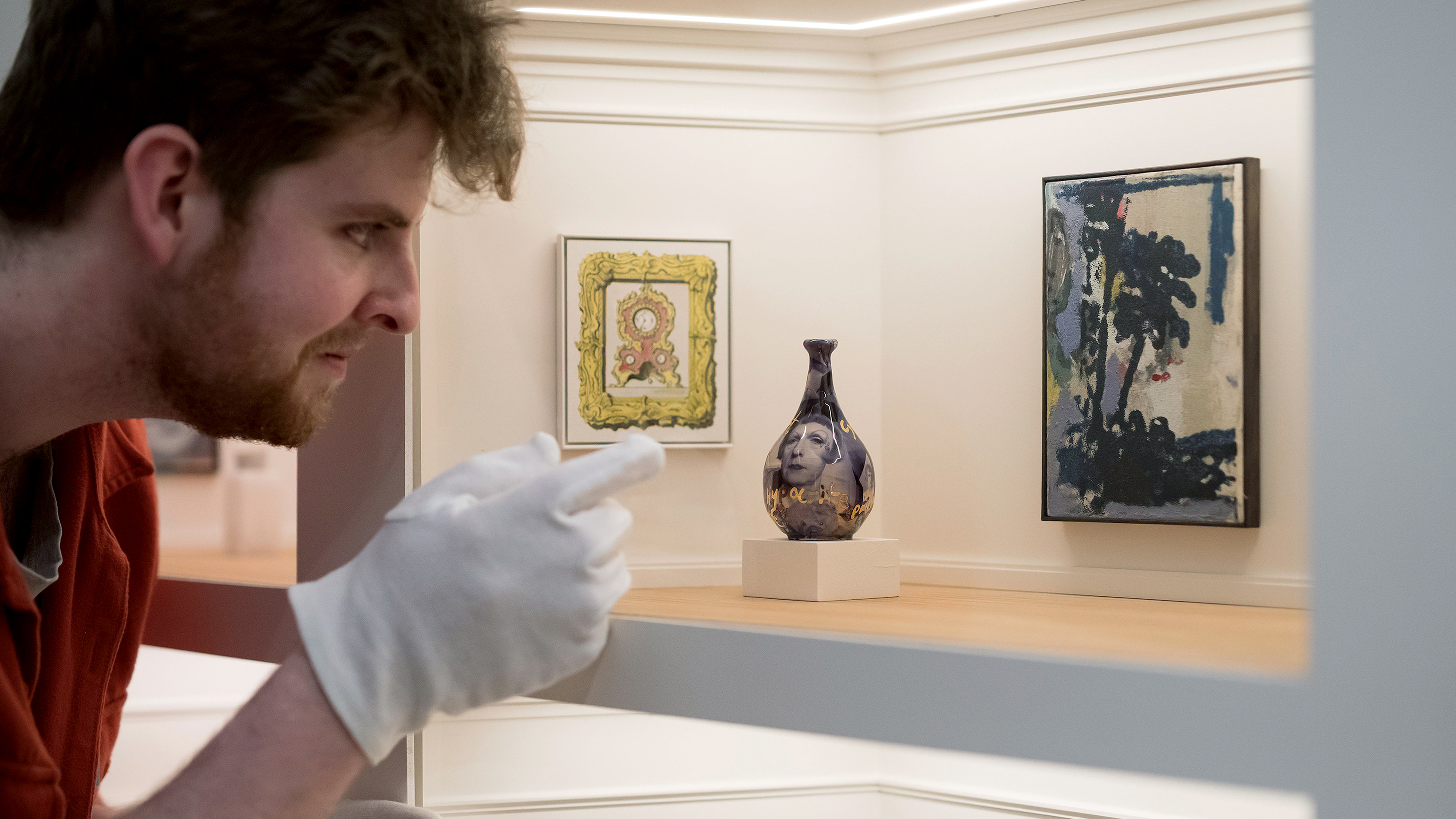 Ein Mann mit Handschuhen betrachtet eine Ausstellung in einer typischen Kunstgalerie mit 80 originalen Miniaturkunstwerken
