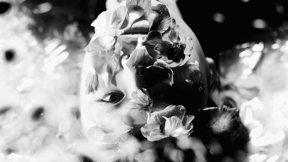 A black and white photo of a woman laying down with flowers on her face