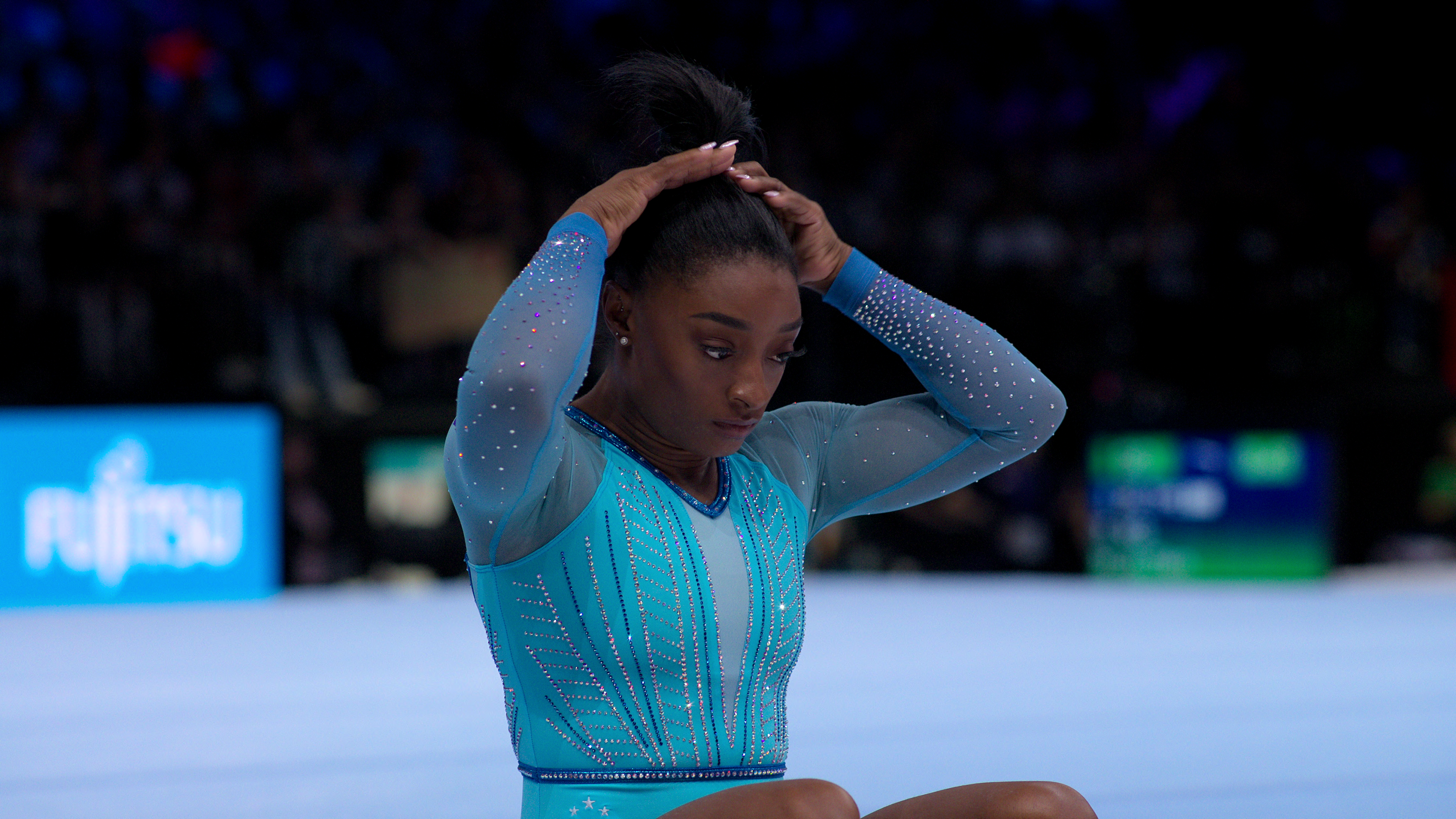 Simone Biles sits in a leotard and adjusts her hair