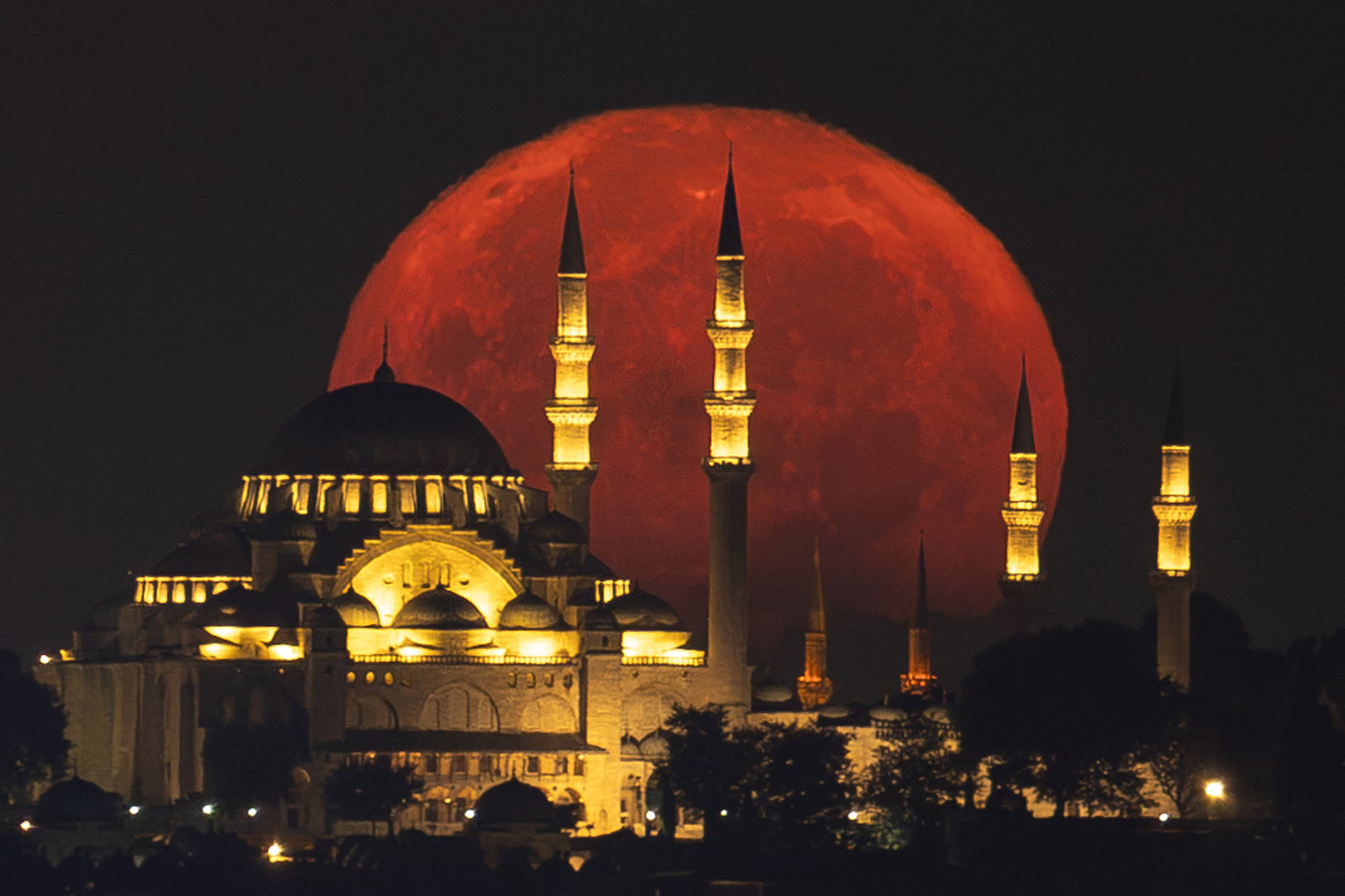 A big red full moon rises above the Suleymaniye Mosque in Istanbul, Turkey