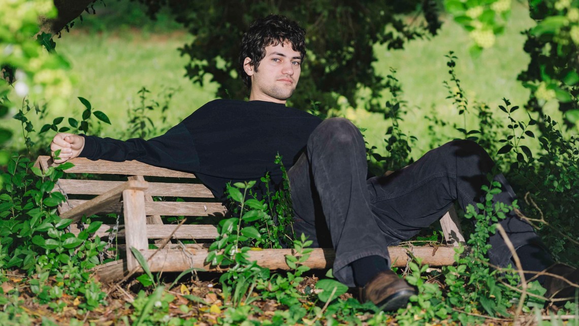 The singer-guitarist MJ Lenderman wears all black and sits on a bench