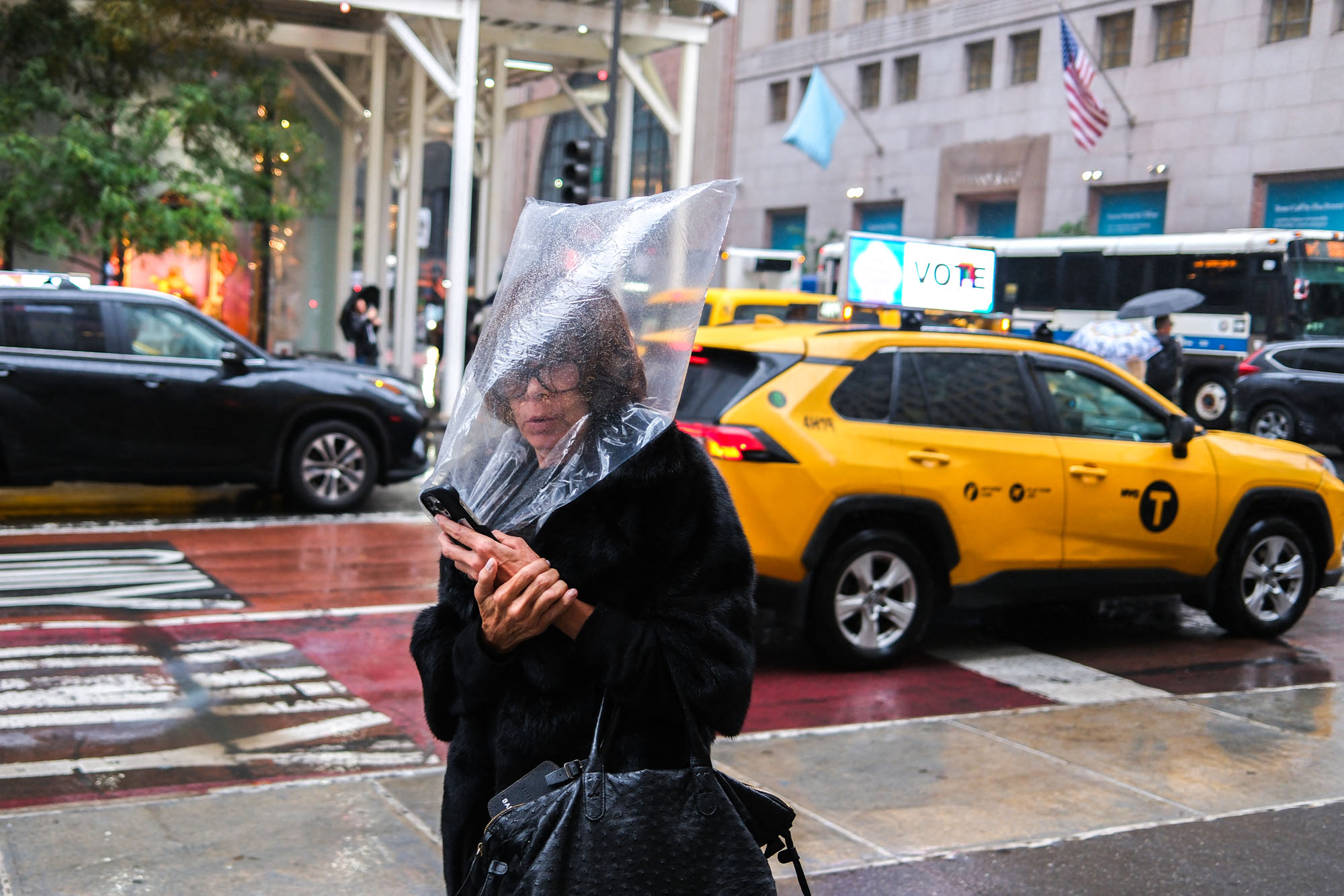 A woman holds a plastic bag over her head to shelter herself from the rain as she walks along Fifth Avenue in New York City.