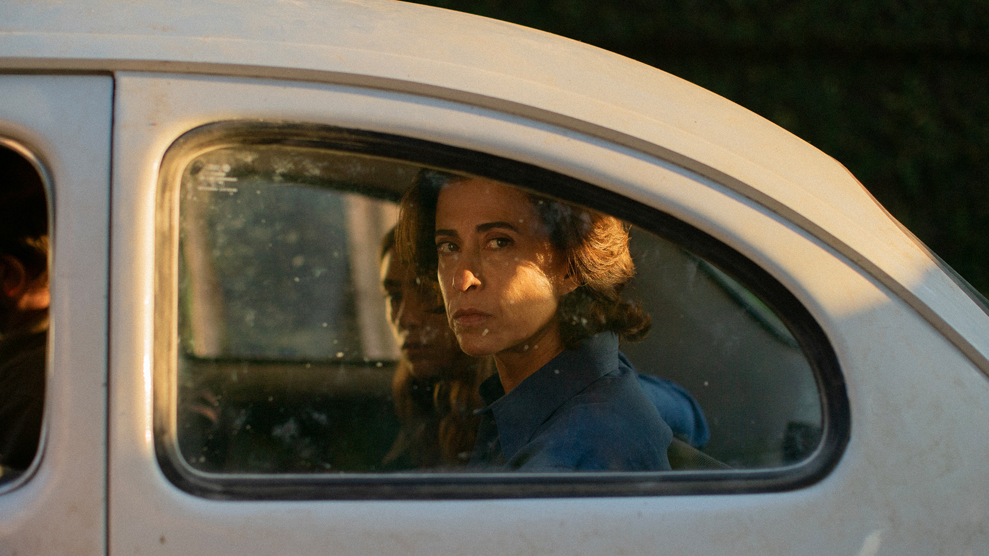 A woman and her daughter look stonily out the window of a car