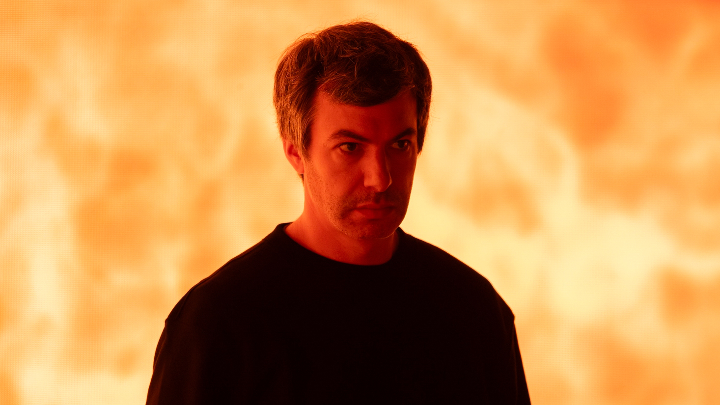 A photo of Nathan Fielder in front of an orange background