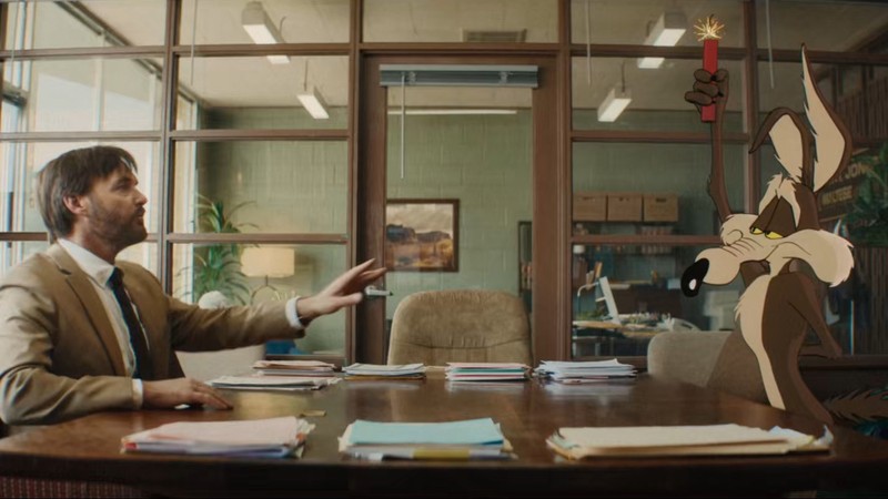 Will Forte sits across a table from the cartoon Wile E. Coyote.
