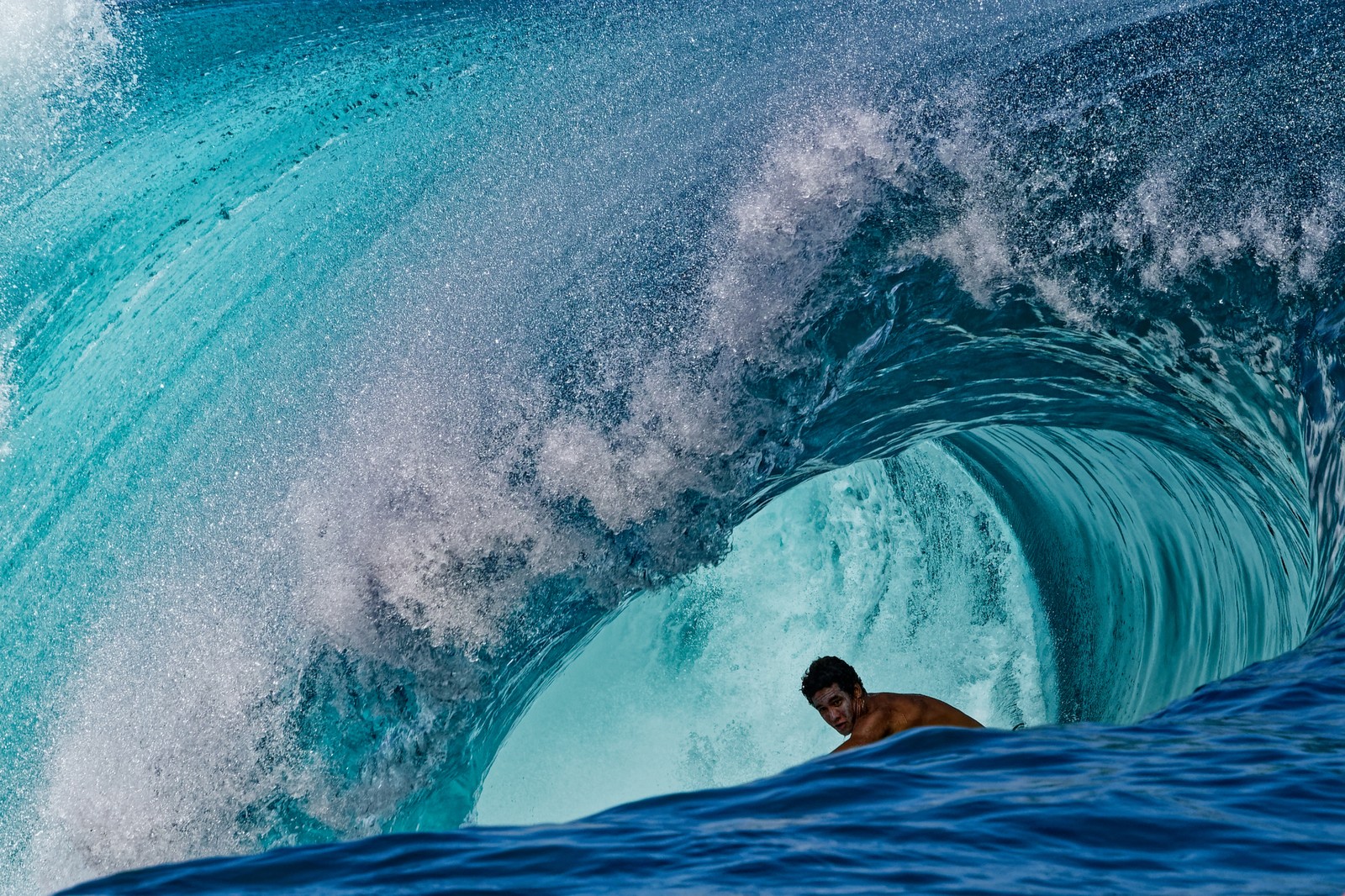 A surfer, seen inside a large curl of a wave.