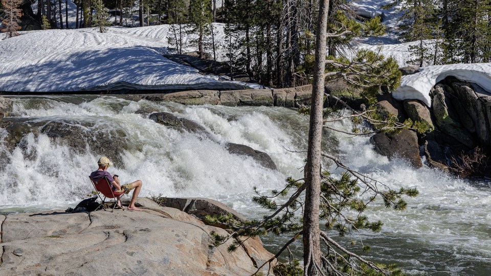 A man reads on the ledge near a stream filled with melting snowpack