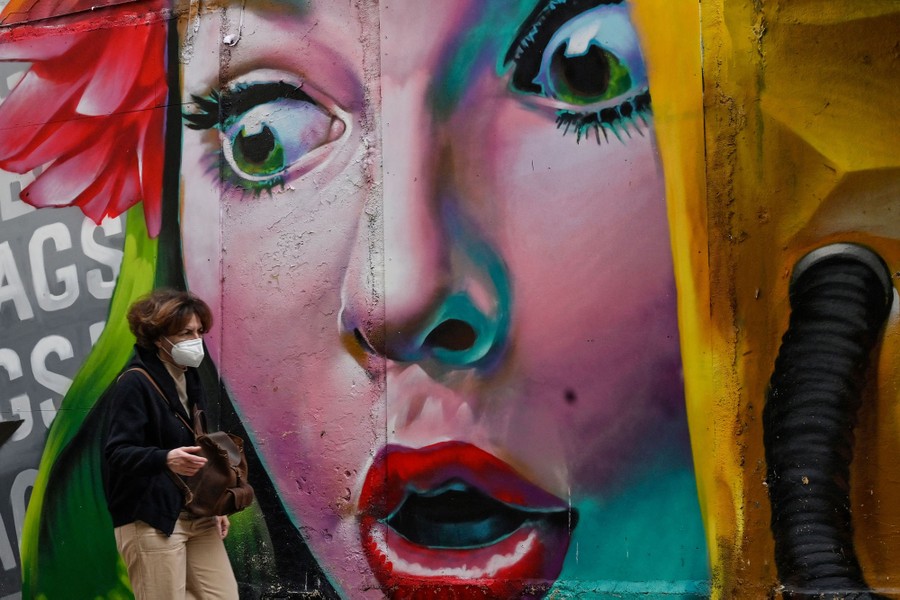 A pedestrian walks past a large mural of a person's face.
