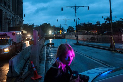 A woman looks at a car next to an ambulance and a flooded tunnel