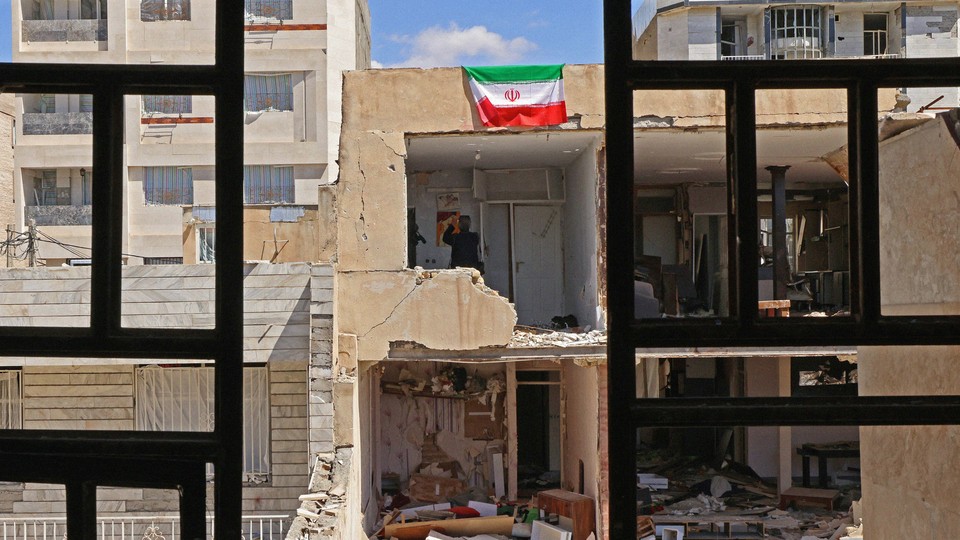 Photograph taken behind iron window grills of a destroyed building with an Iranian flag hanging from its side