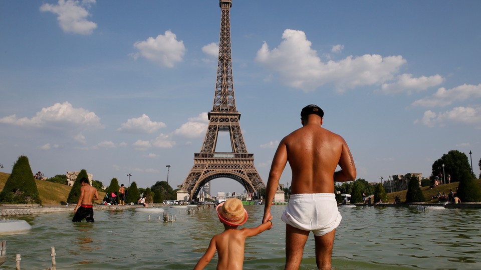 A man and a young child with sunburned bodies stand in a pool of water in front of the Eiffel Tower.