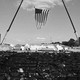 A black-and-white photograph of a large American flag being hung vertically over the stage of Donald Trump's Pennsylvania rally