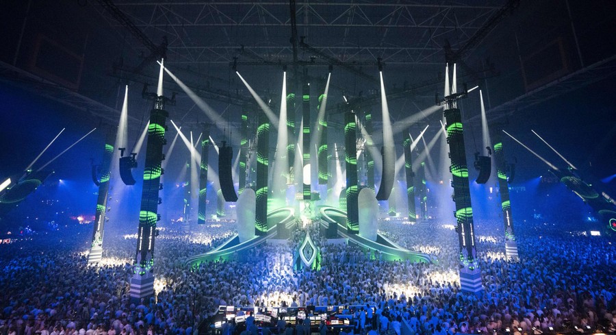 Thousands of concertgoers gather in front of a large stage in an arena.