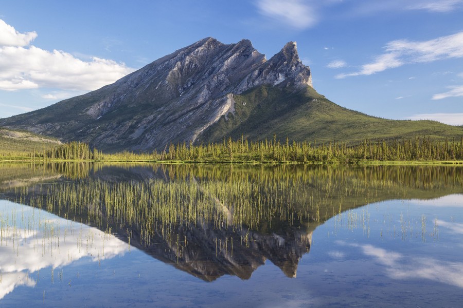 An angular, rocky mountain stands reflected in a nearby lake.