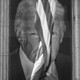 A banner with President Trump's image on it, hanging between building columns with an American flag flying between his eyes.