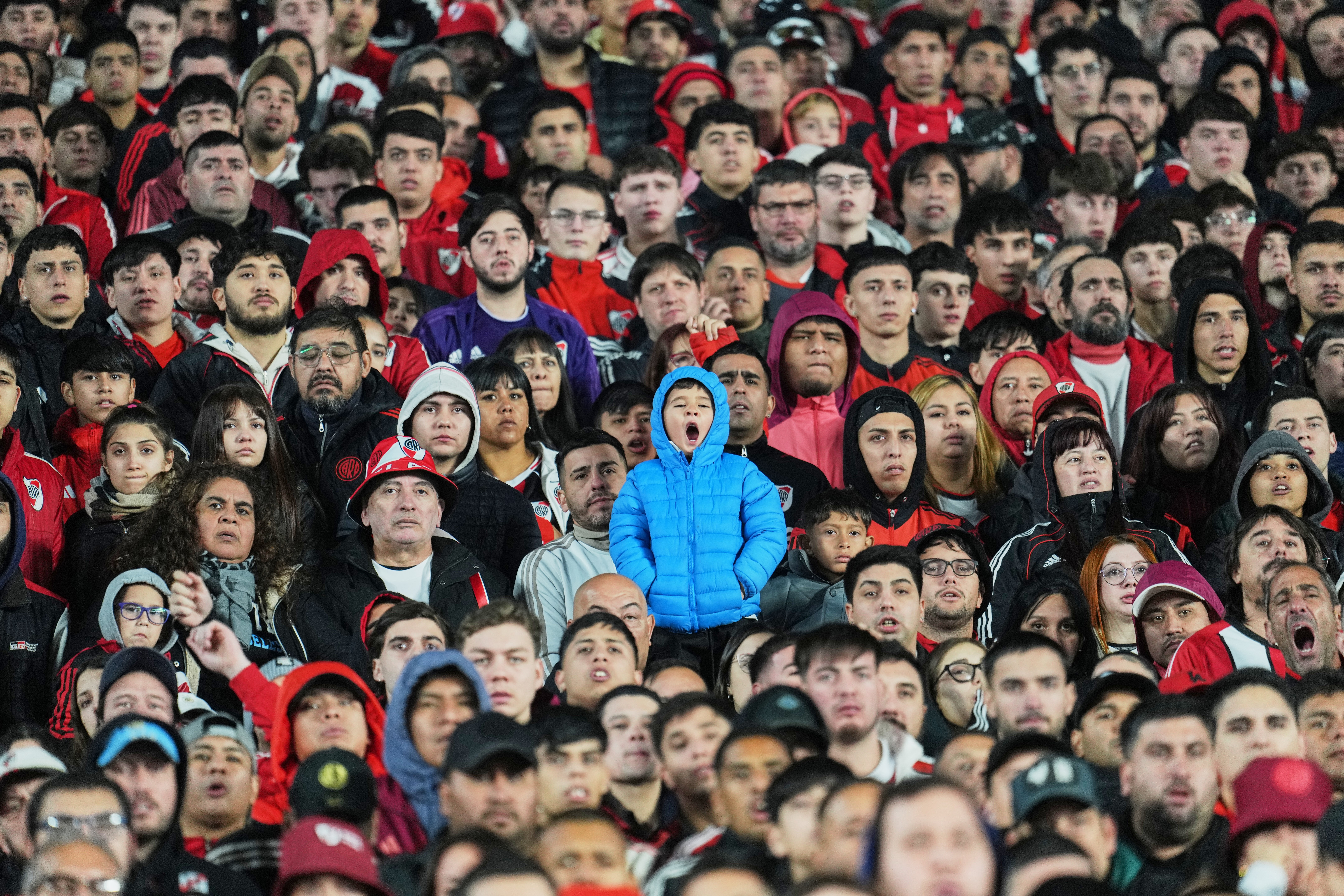 A child stands among many seated soccer fans in a stadium.