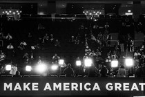 Attendees at the 2024 Republican National Convention sit in the audience, behind a row of bright lights and a banner reading "Make America great"