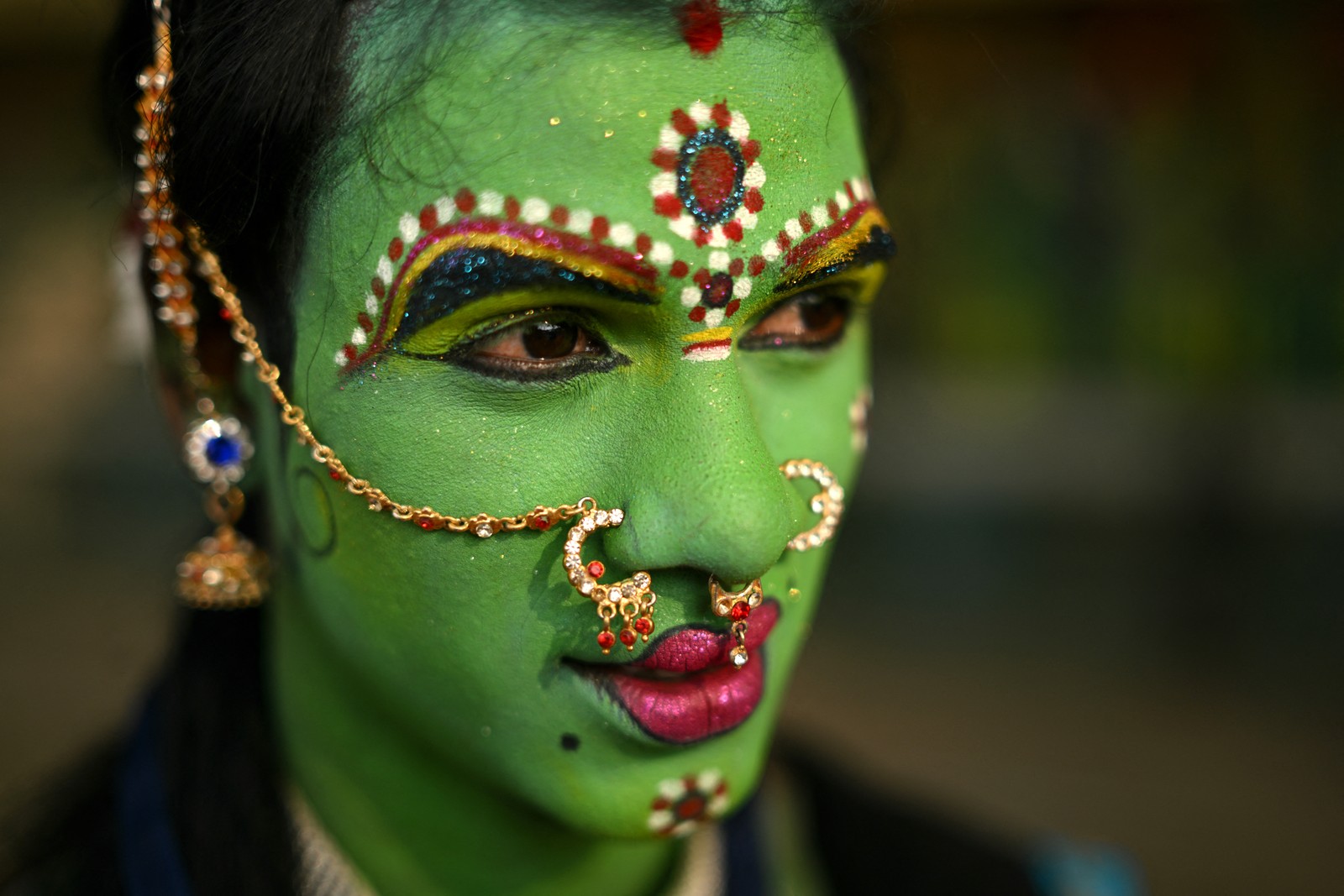 A person poses while wearing ornately decorated green make up on their face.