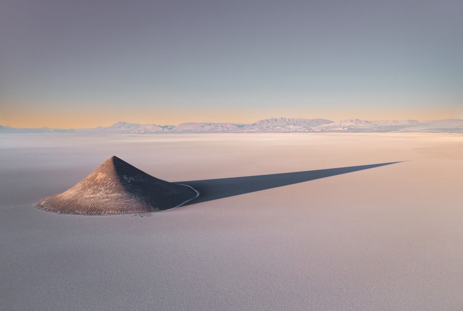 A lone conical hill stands in a broad salt plain