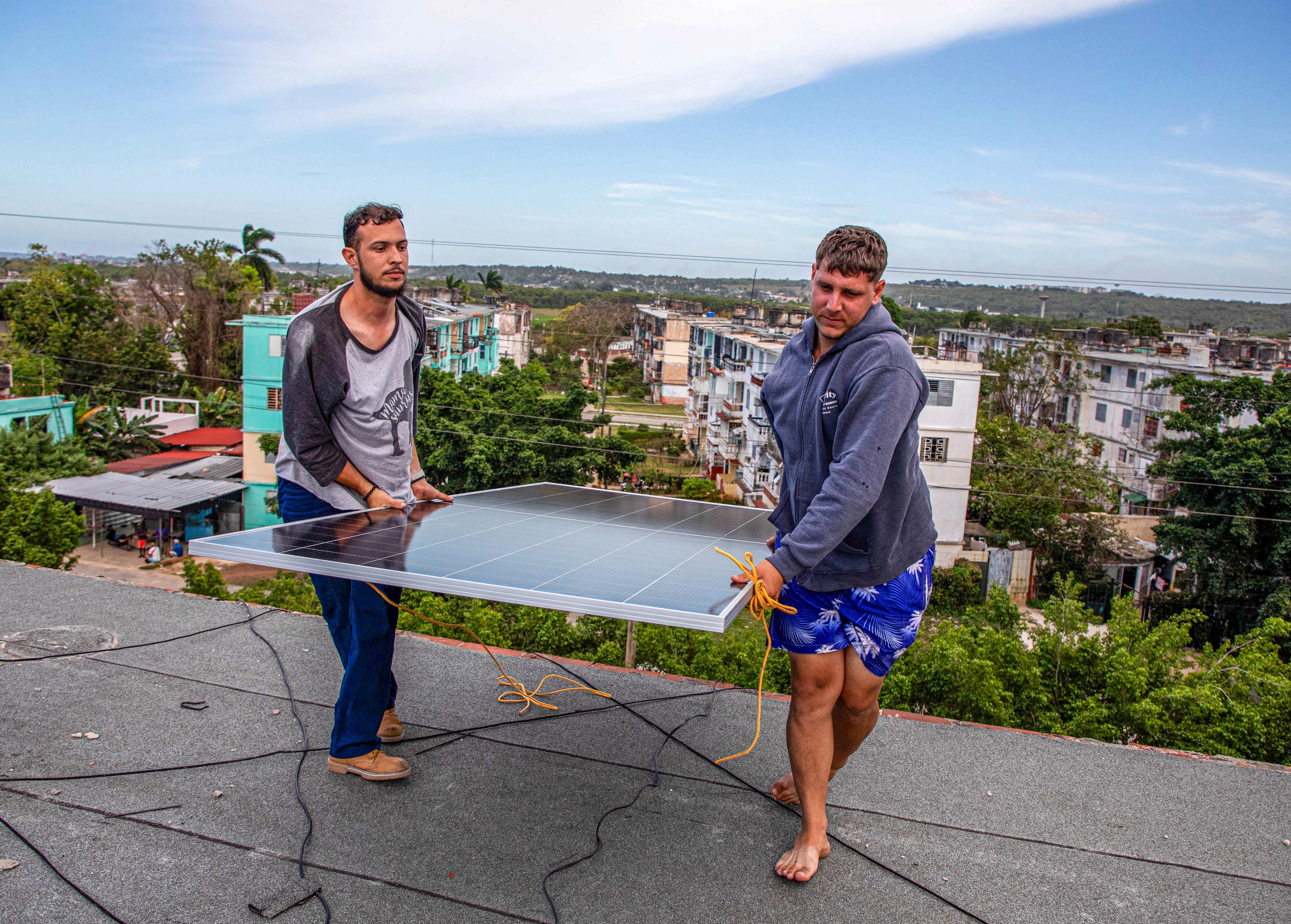 Two solar-panel specialists install a panel on a rooftop.