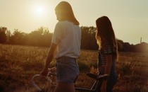 Two friends walking with a bike in a field