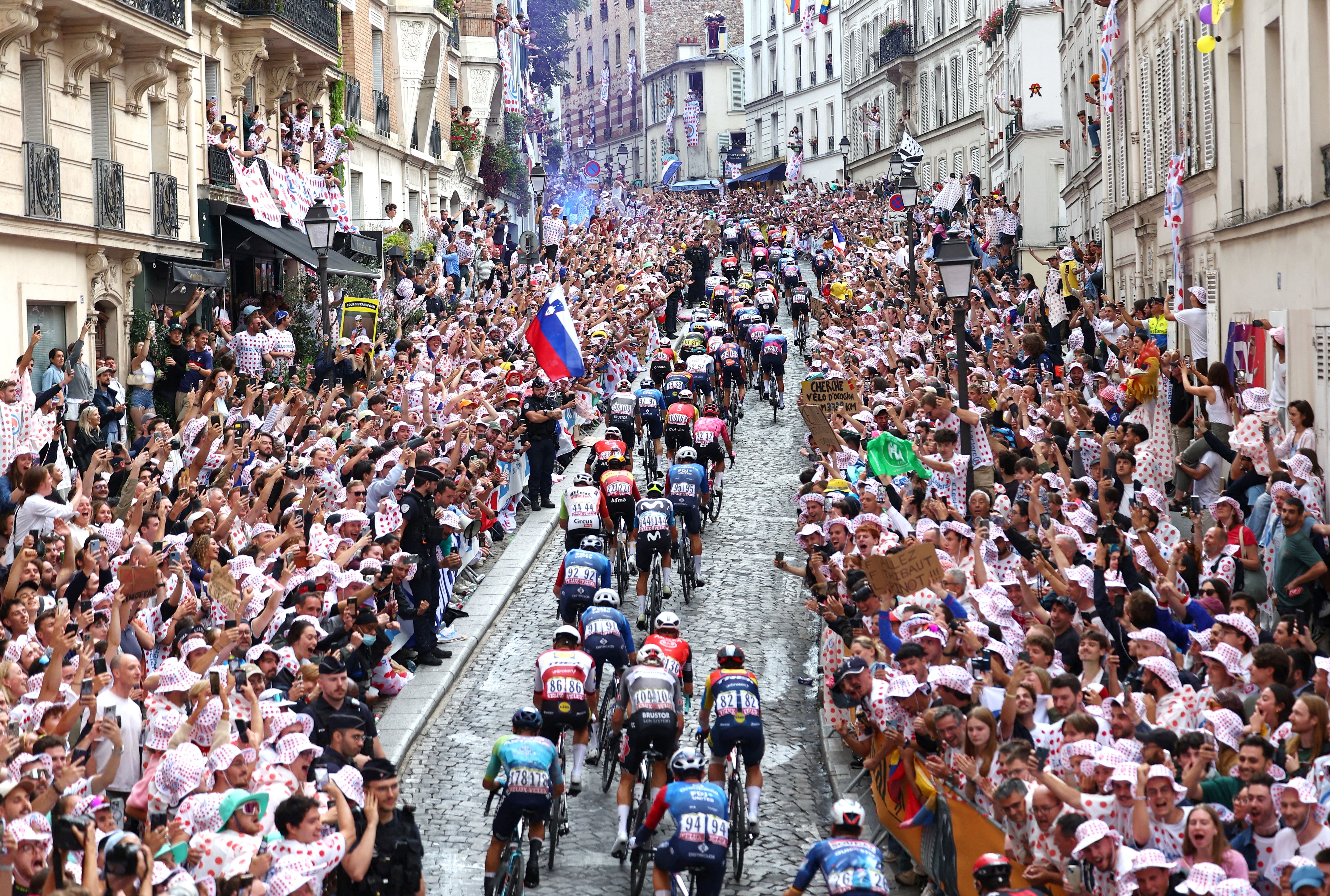Crowds on either side of a city street cheer racing cyclists as they ride past.