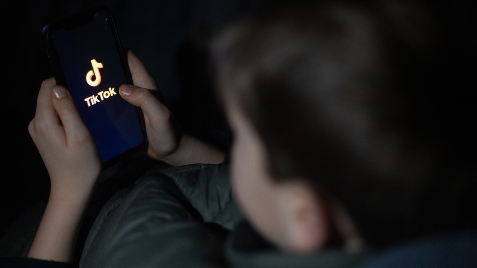 A 12-year-old boy looks at a smartphone screen displaying the TikTok logo