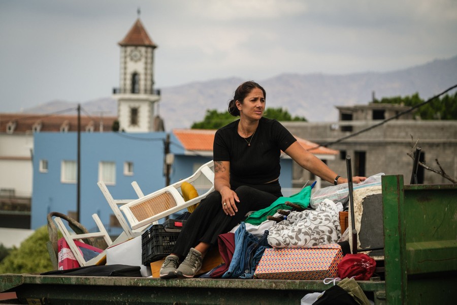 A woman sits atop a pile of belongings in the back of a truck.