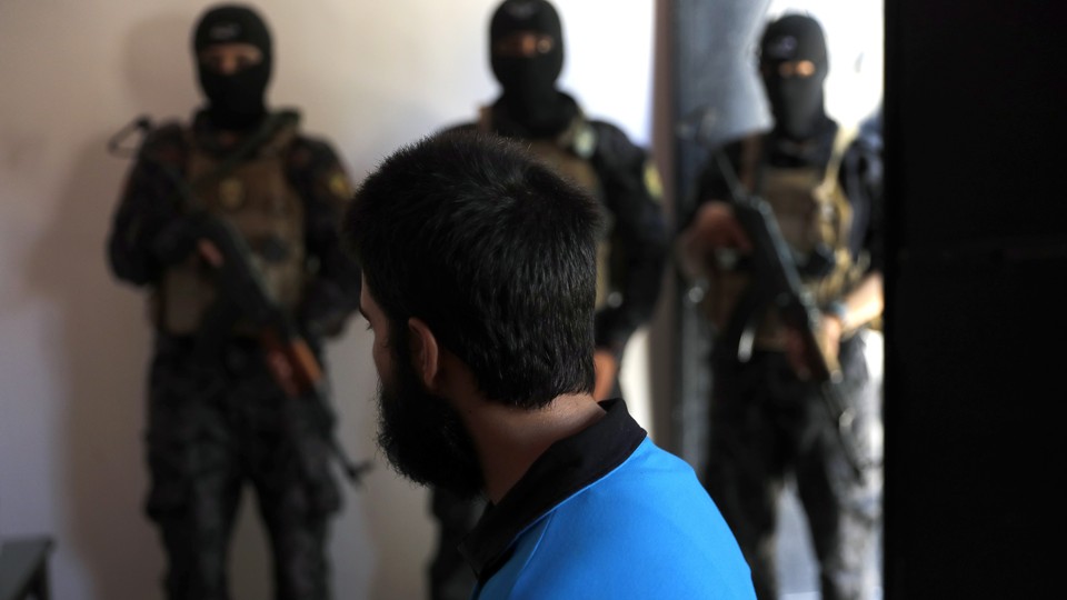 Kurdish soldiers from the Anti-Terrorism Units stand in front a suspected Islamic State member 