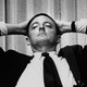 William F. Buckley sits with his hands placed behind his head.
