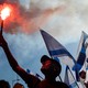 A protester lifting a torch in a crowd of people holding Israeli flags