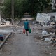 Photo of a woman walking down a road in Ukraine with debris and destroyed buildings around her.