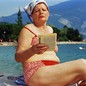 A woman in a kerchief and red bikini reads a book on a beach.
