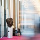 A blurred color photo of the Grand Foyer of the Kennedy Center, showing a bronze bust of John F. Kennedy in focus.