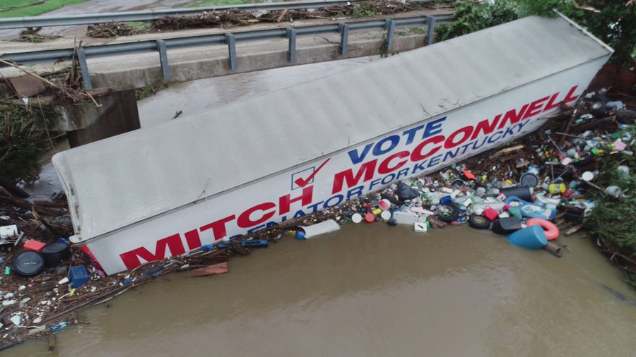 A tractor trailer with the words "Vote Mitch McConnell" written on the side sits in a flooded creek, pushed against a bridge.