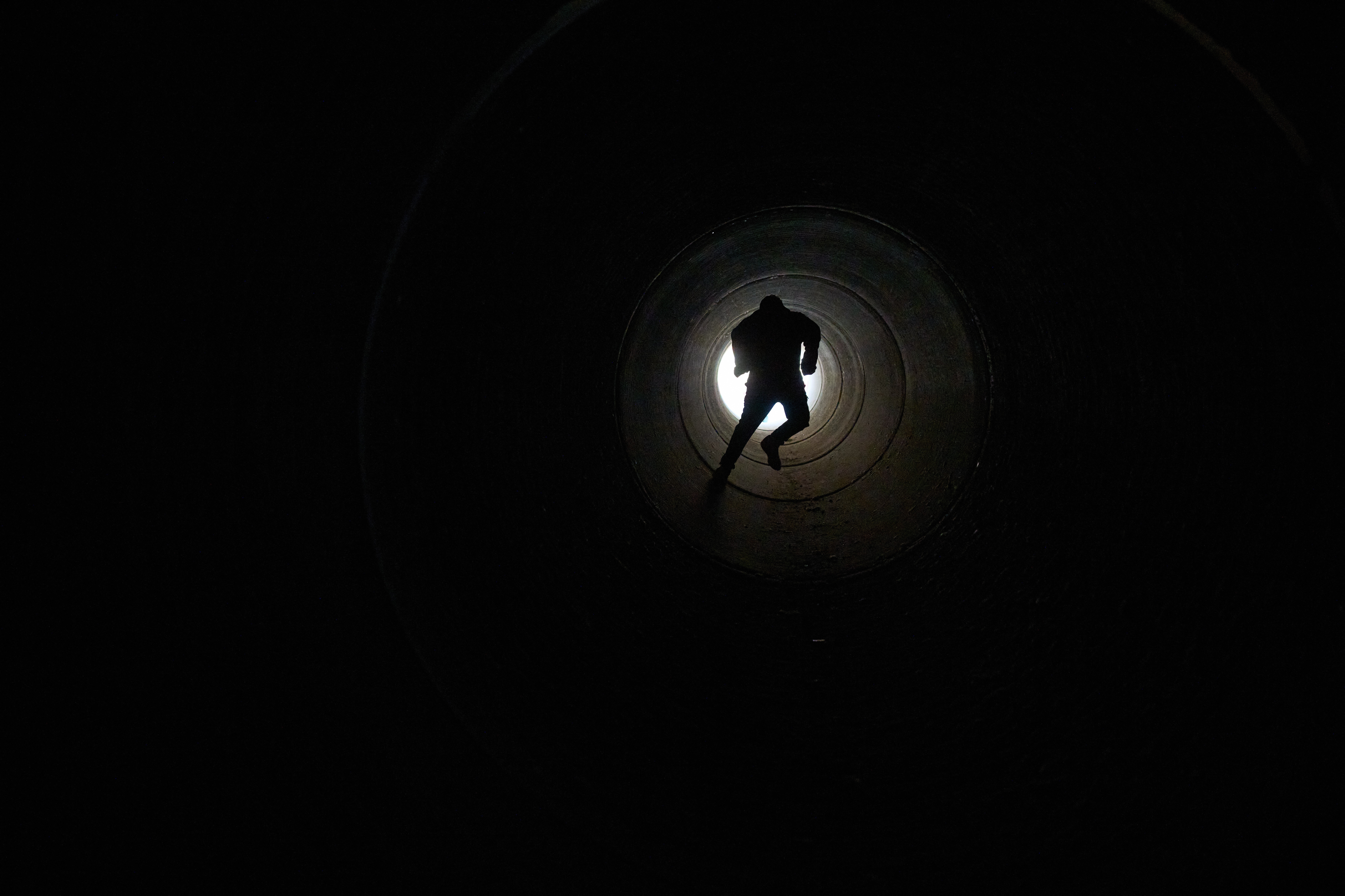A boy runs inside a large cement pipe, seen from inside.