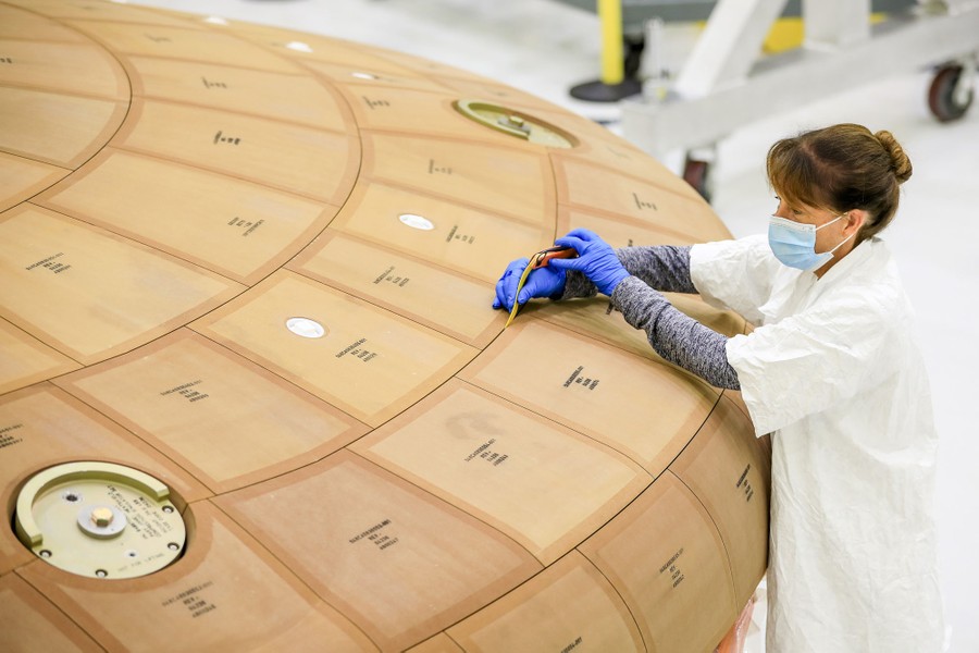 A person measures the gaps between tiles on a spacecraft's heat shield.