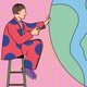 A man sits on a stool in front of a large globe, looking for a place to put a pin with a smiley face on it