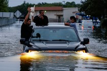 Three people hang onto the outside of a truck as it travels through floodwaters in Houston.