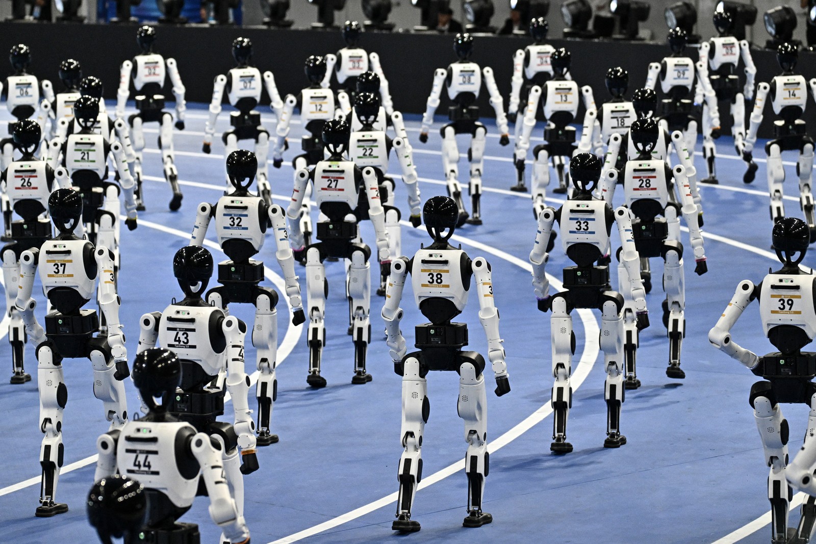 Dozens of robots parade on an indoor track.
