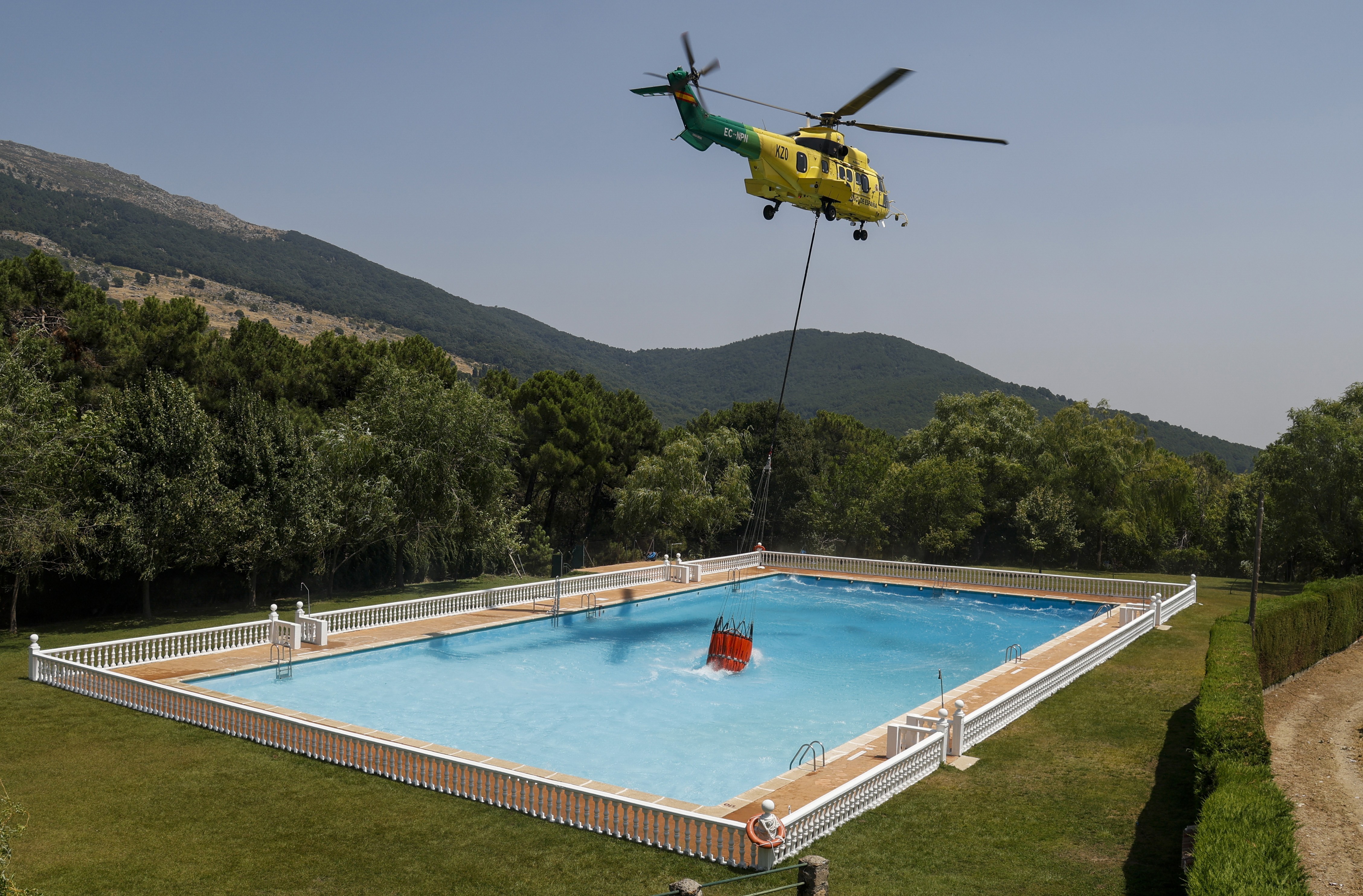 A helicopter uses a bucket hanging from a cable to collect water from a swimming pool to combat wildfires.