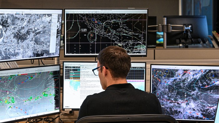 A man sits in front of 5 screens analyzing weather patterns