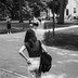 A black-and-white photo of a young woman, seen from behind, wearing a backpack and walking on a campus