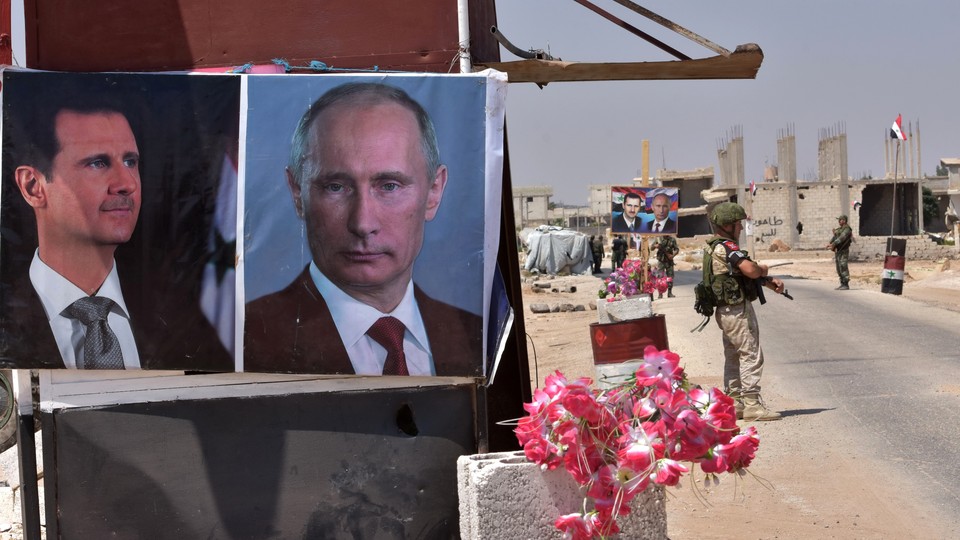 Flowers lie next to posters of Assad and Putin in Idlib.