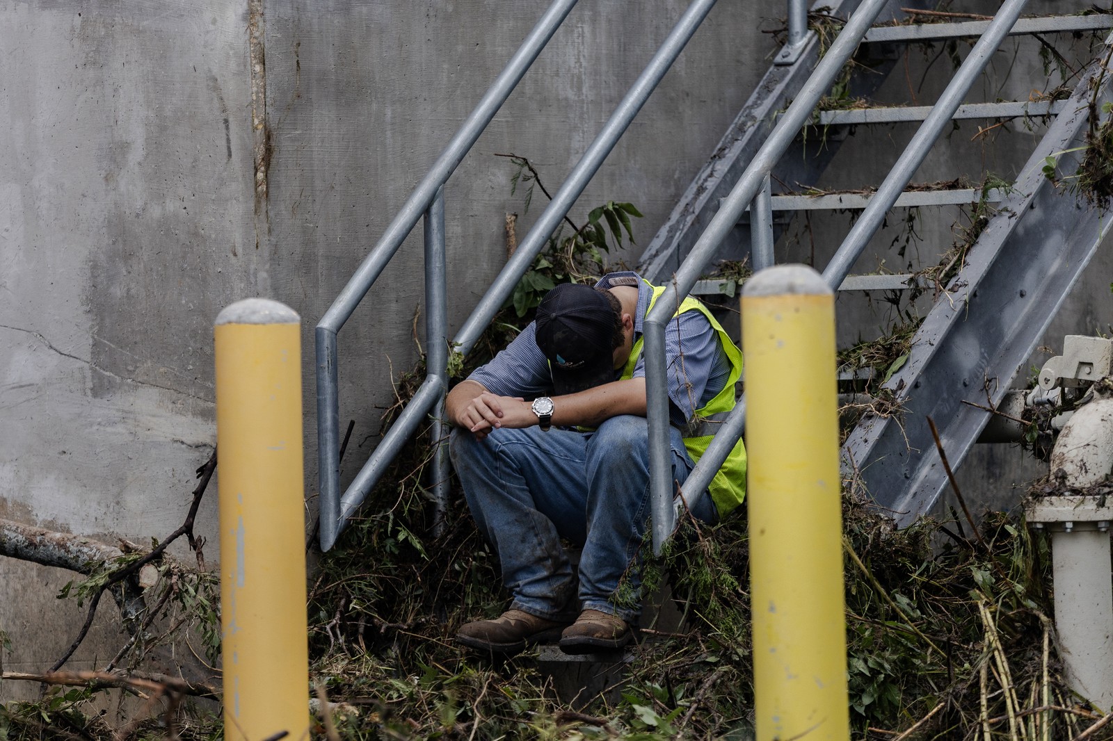 A cleanup crew worker sits at the bottom of an exterior staircase, resting.